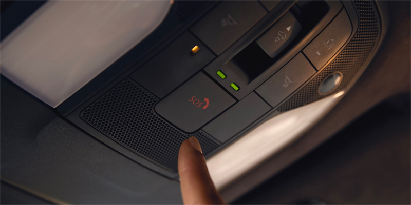 A hand pressing the red SOS button on a 2025 INFINITI QX50 SUV's overhead control panel.